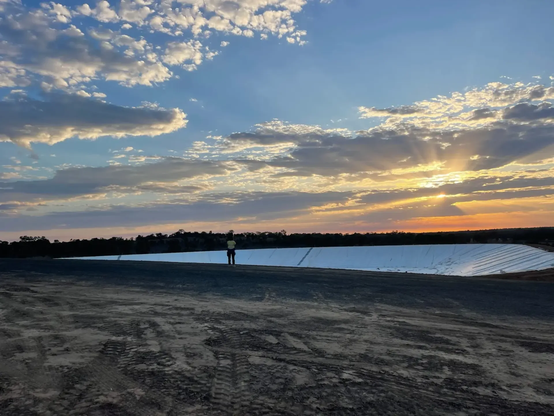 Lined water containment pond at sunset with a worker standing on the crest